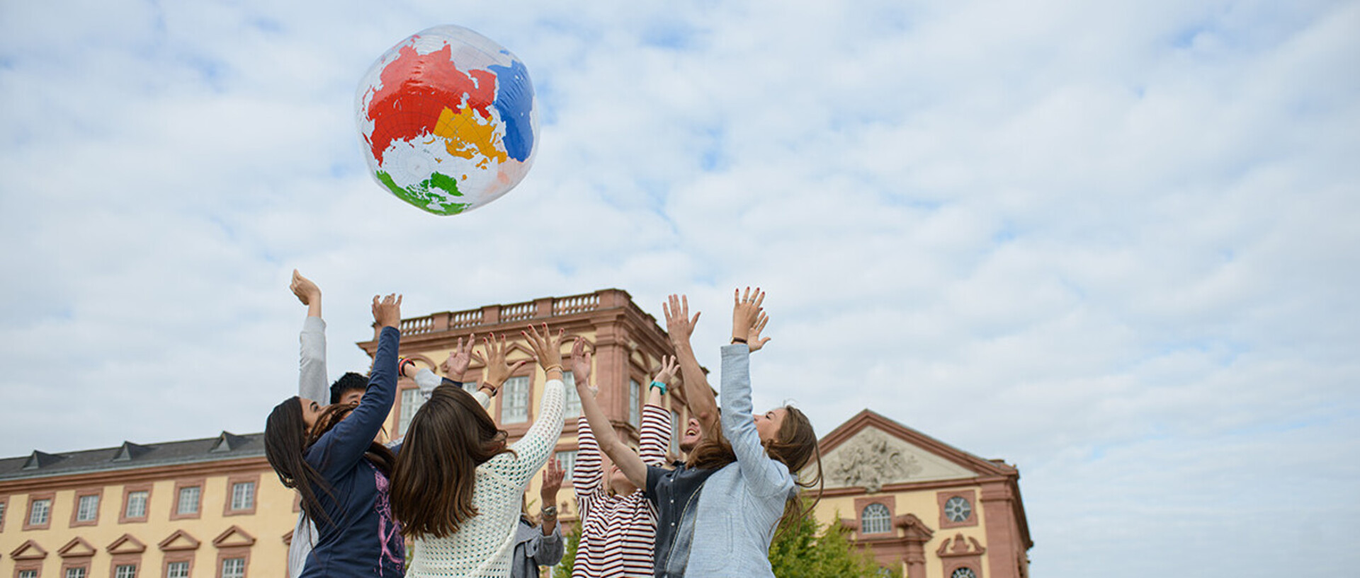 Eine Gruppe Studierender wirft einen aufgeblasenen Globus in die Luft. Dahinter ist das Schloss zu sehen.