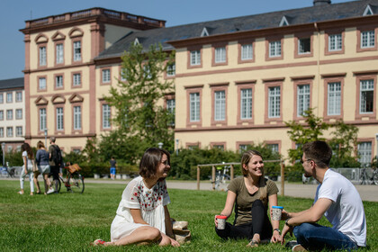 Drei Studierende sitzen auf der Mensawiese der Universität Mannheim und unterhalten sich.