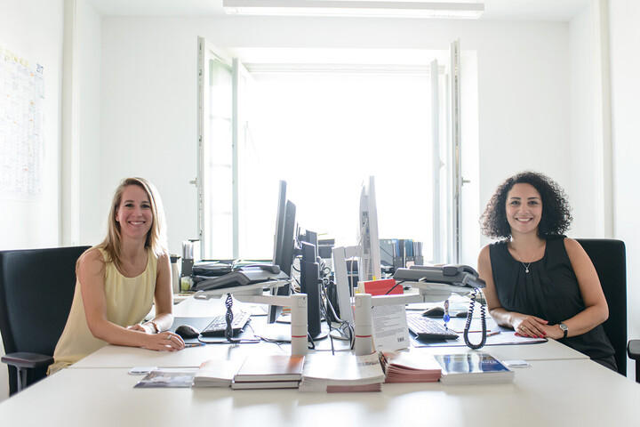 Zwei  Mitarbeiterinnen sitzen im Büro vor ihren Computern