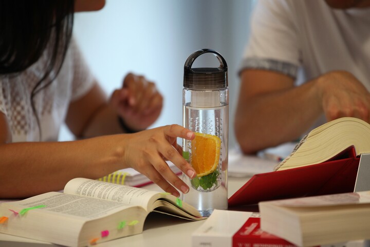 Zwei aufgeschlagene Gesetzesbücher auf einem Tisch, die Hände zweier Studierender sind  zu sehen
