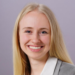Porträt von Alena Lennartz. Sie trägt ein graues Sakko, dazu ein weißes Hemd.