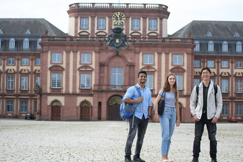 Drei Studierende auf dem Ehrenhof gucken in Richtung Kamera. Im Hintergrund der Mittelbau des Schlosses.