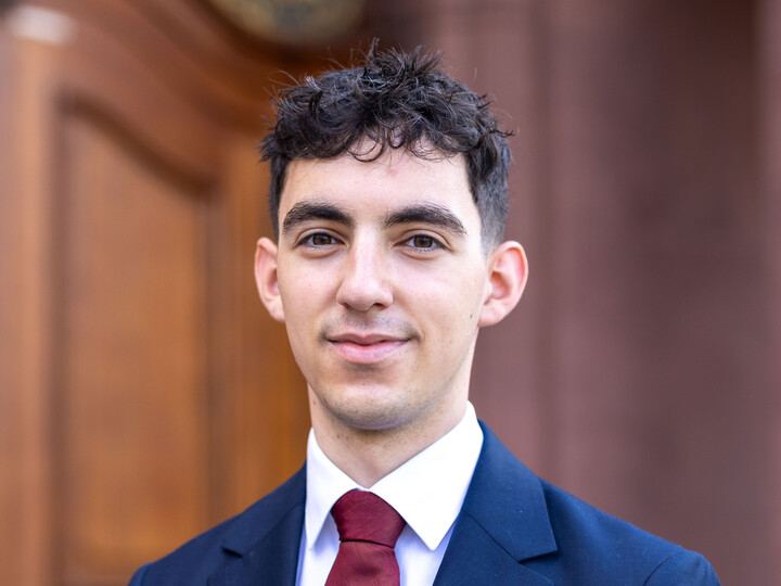 Stefanos Hatzianastassiou trägt einen blauen Anzug. Er lächelt in die Kamera.