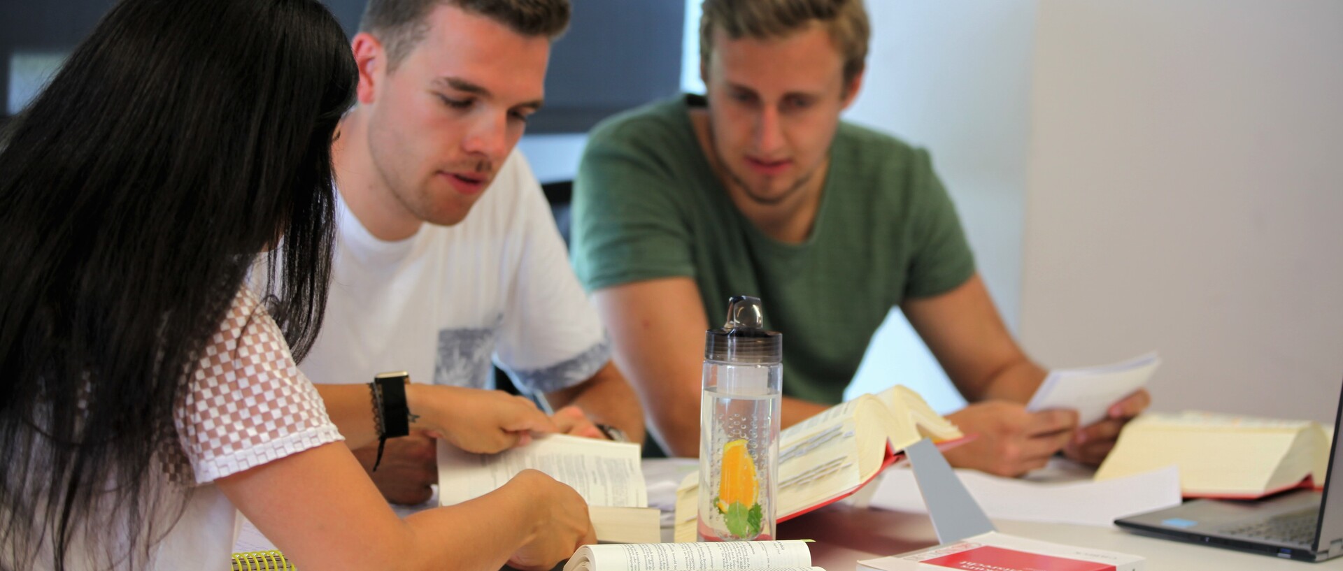 Drei Studierende am Tisch, mit aufgeschlagenen Büchern und Notizen