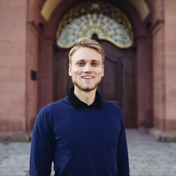 Tom Kranz in blauem Pullover vor dem Schloss