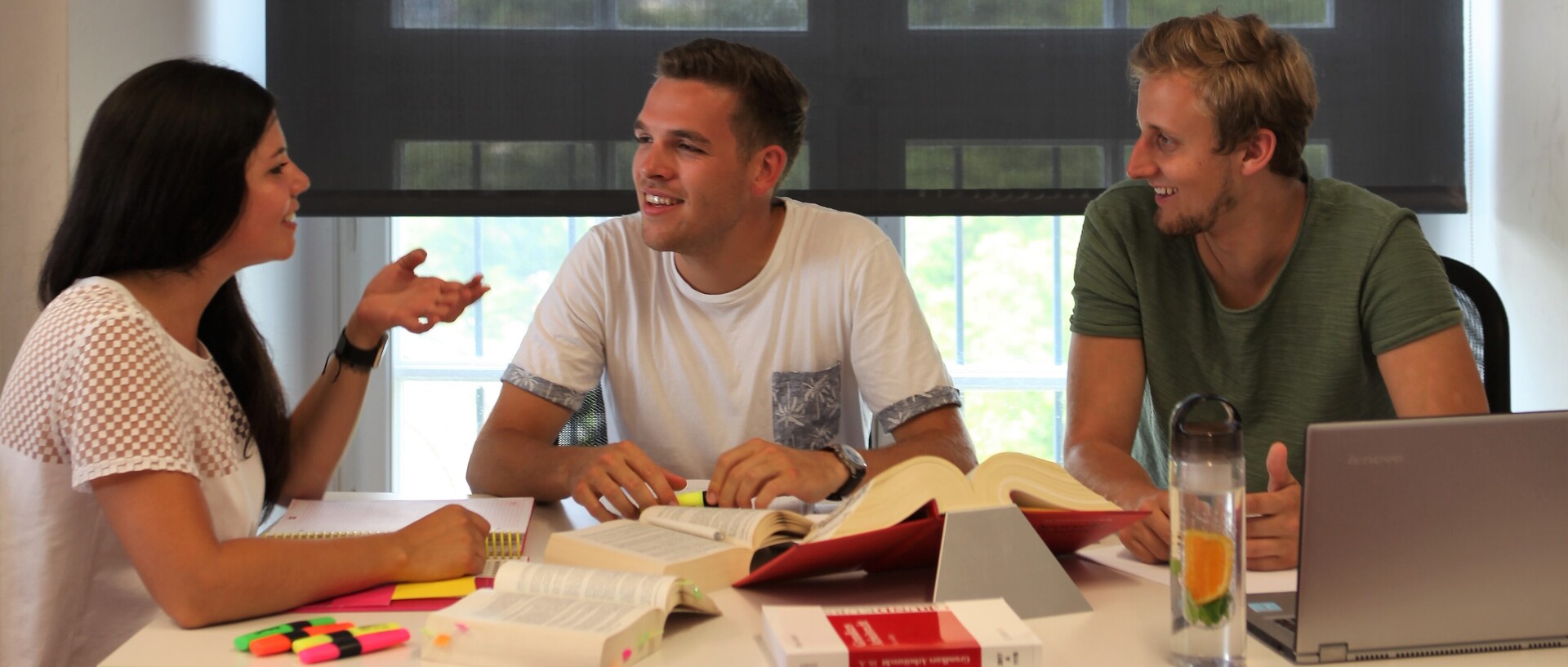 Eine Gruppe Studierender sitzt an einem Tisch mit aufgeschlagenen Büchern und unterhält sich