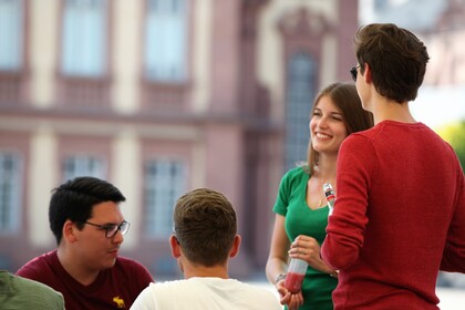 4 Studierende vor dem Schloss. Sie lächeln. Sie unterhalten sich.