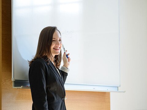 Eine Frau steht vor einem Whiteboard und zeigt lächelnd auf etwas