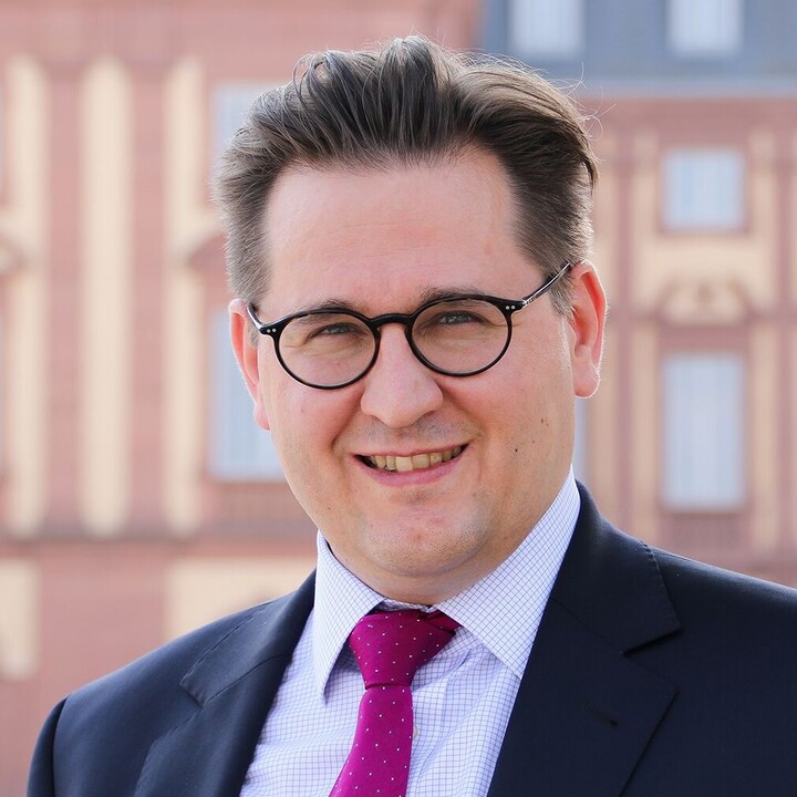 Friedemann Kainer in black suit and red tie outside palace