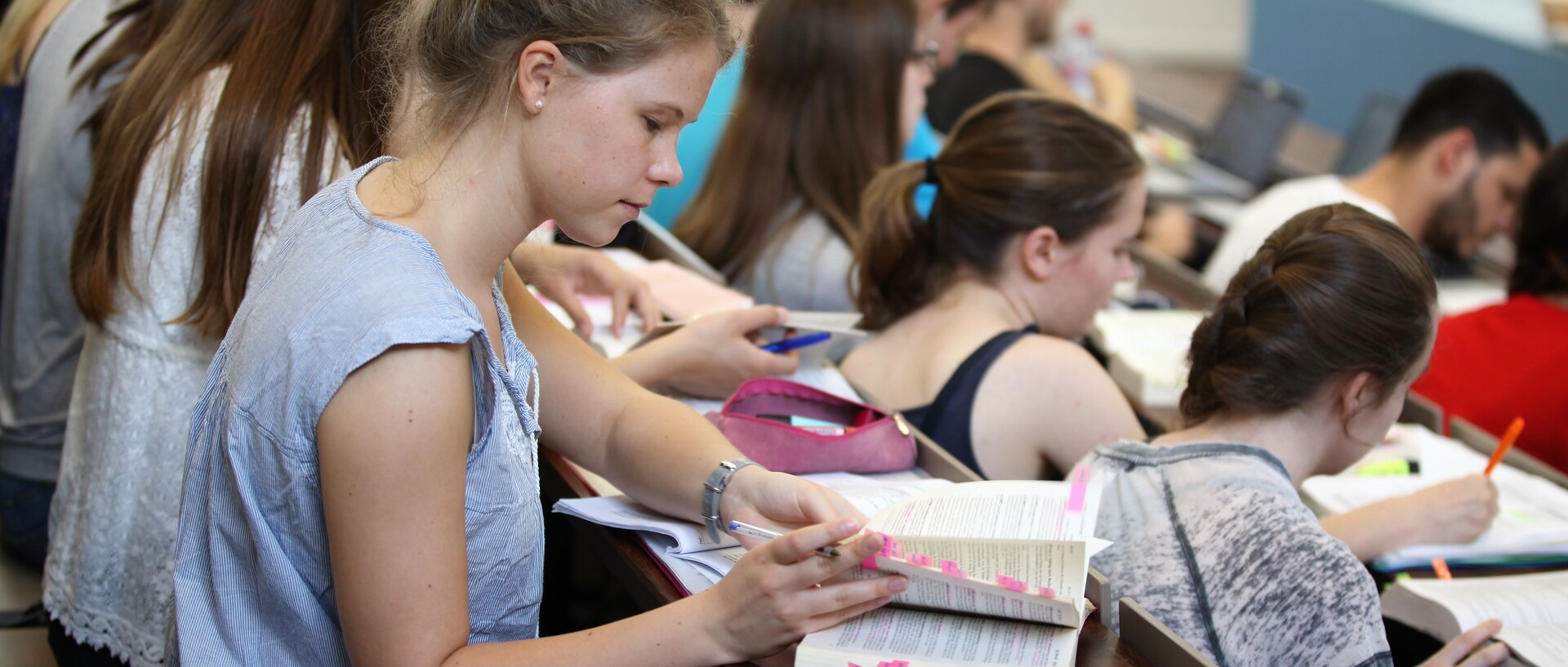 Studierende in Hörsaal mit aufgeklappten Büchern und Notizbüchern