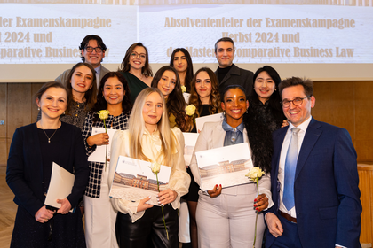 Gruppe von Absolventinnen und Absolventen sowie von Frau Dr. Fischinger-Corbo und Herrn Prof. Dr. Kainer in der Aula des Schlosses. Sie lächeln alle.