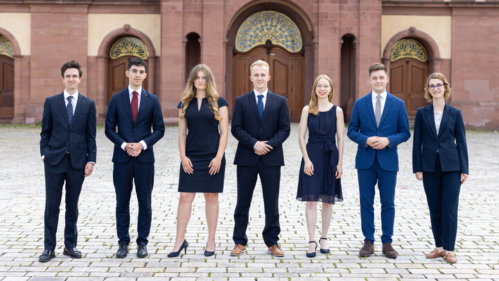 Eine Gruppe Studierender steht in Anzügen vor der Universität Mannheim.