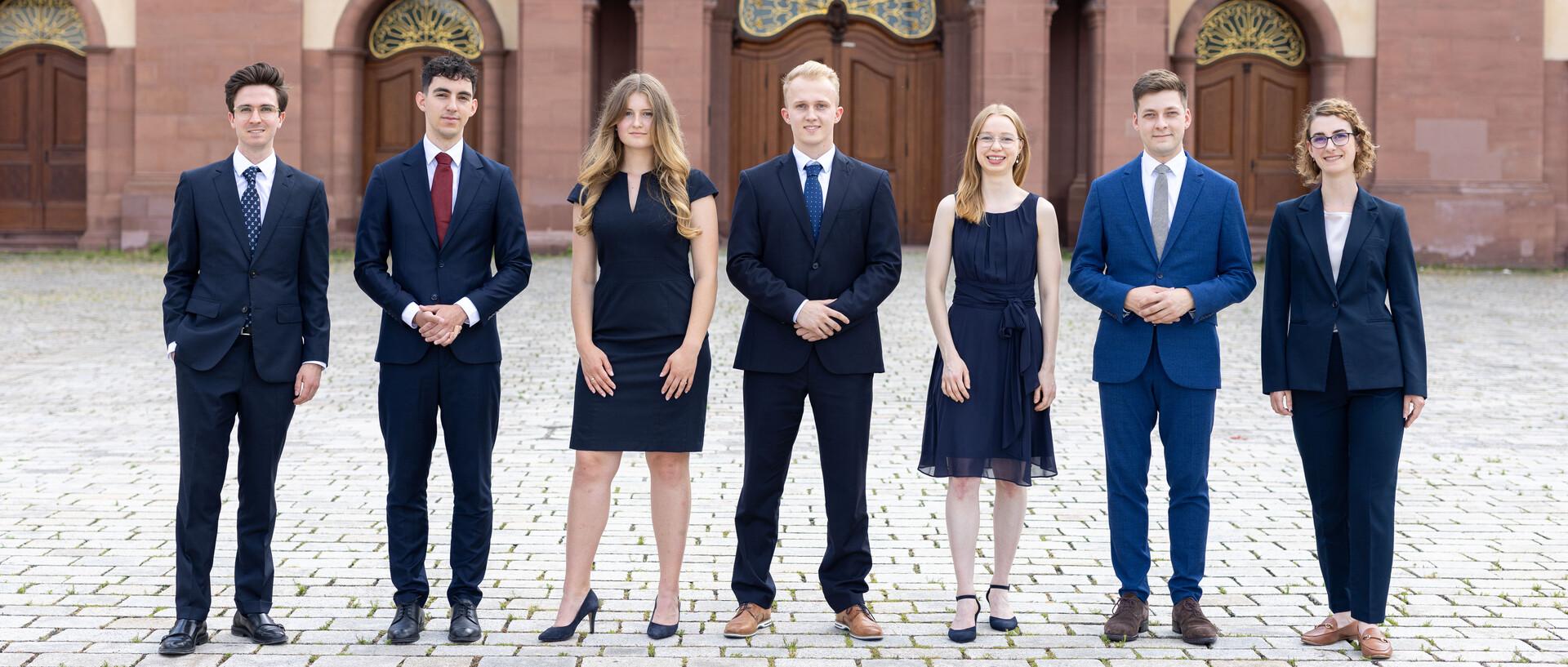 Eine Gruppe Studierender steht in Anzügen vor der Universität Mannheim.