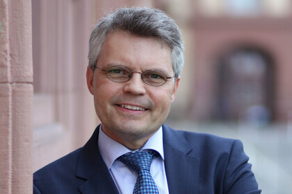 Ralf Müller-Terpitz trägt einen dunkelblauen Anzug mit Krawatte. 