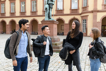 Vier Studierende unterhalten sich im Ehrenhof des Schlosses