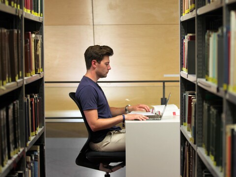Student sitting at a table in the library with laptop