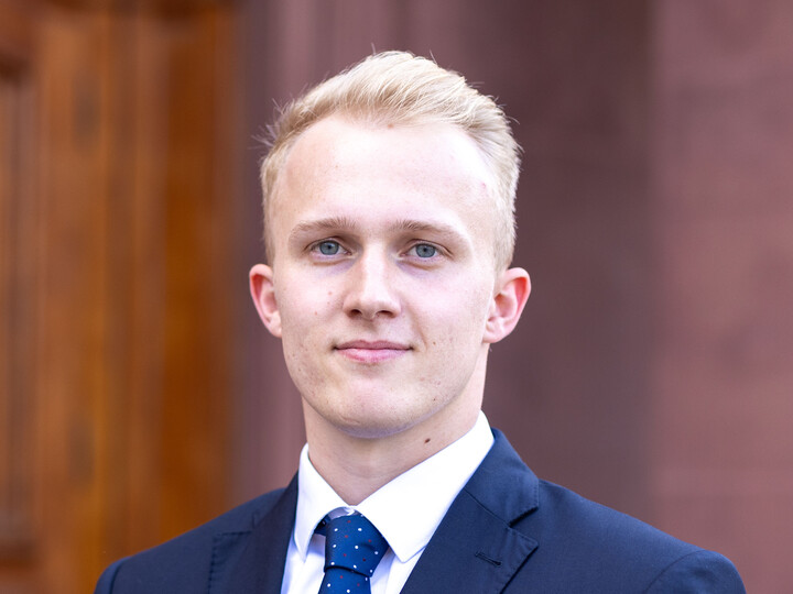 Student im Anzug lächelt in die Kamera.
