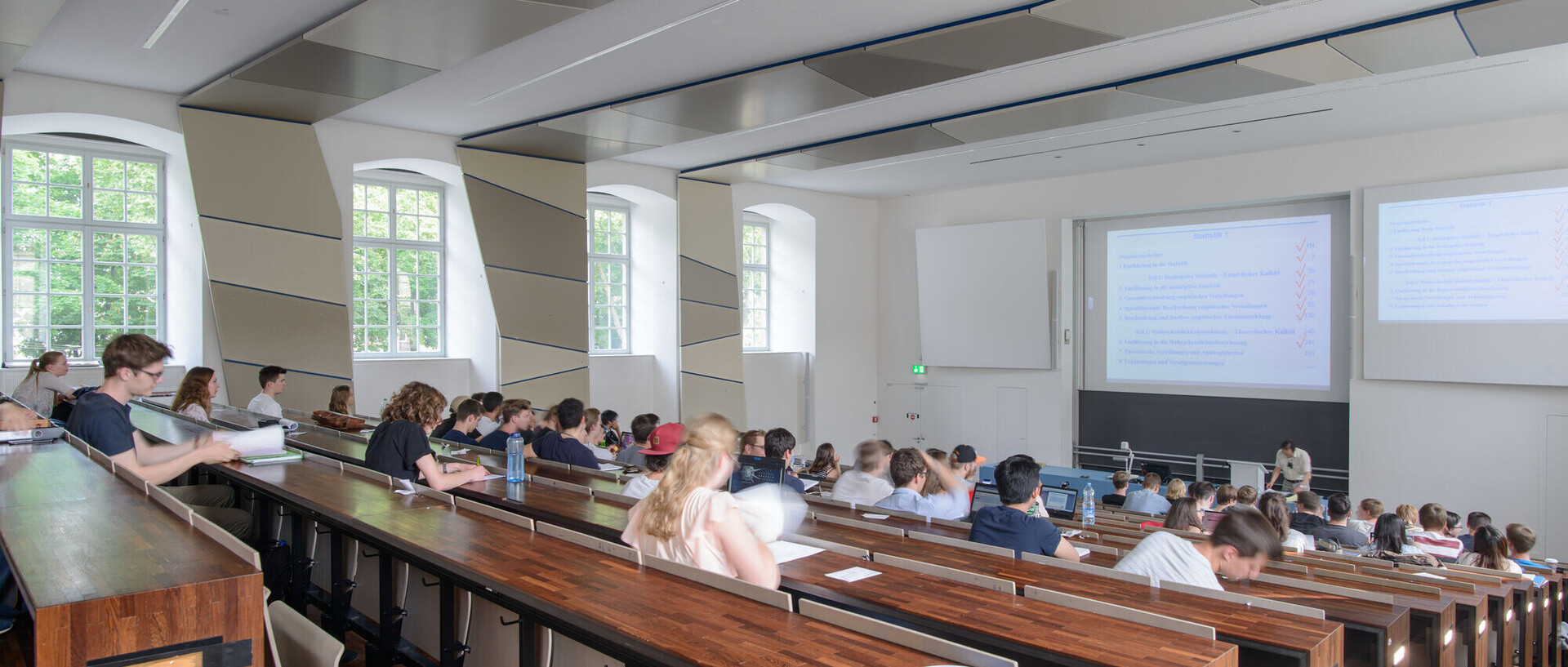 Studenten sitzen in einem Hörsaal und ein Professor hält eine Vorlesung.