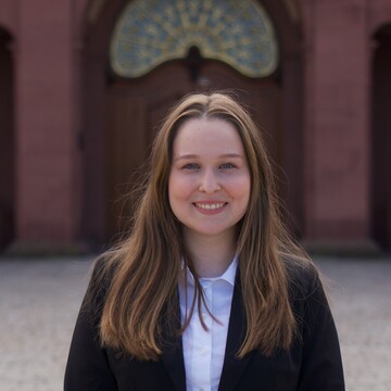 Wissenschaftliche Mitarbeiterin Chiara Rode. Sie trägt eine weiße Bluse und eine dunkle Jacke.